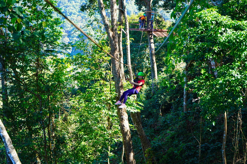Forest Zipline Adventure at Kingkong Smile Zipline Person with green helmet flying on zipline through lush green trees at Kingkong Smile Zipline.