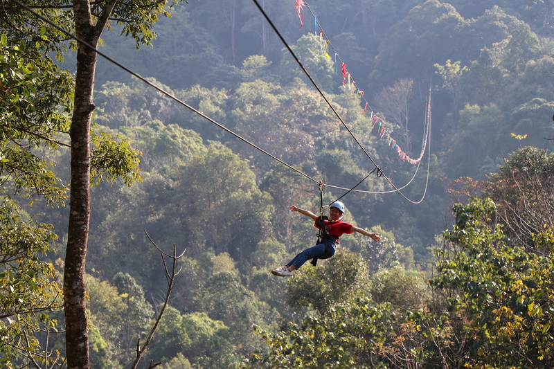 Child in helmet ziplining through lush green forest canopy at Kingkong Smile Zipline.
