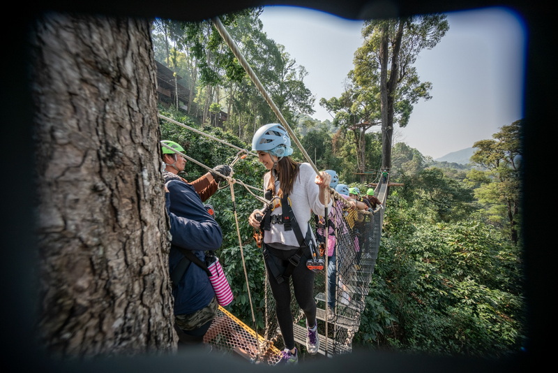 Group of people in helmets crossing a suspension bridge in a lush forest at King Kong Smile Zipline.