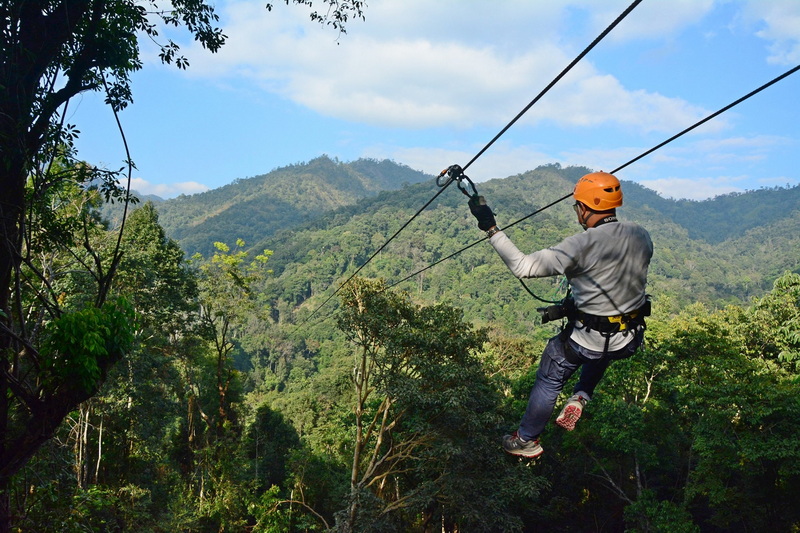 Ziplining Adventure in the Forest at Kingkong Smile Zipline Person ziplining through dense green forest with mountains in the background at Kingkong Smile Zipline.