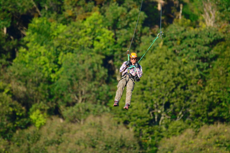 Person in safety gear ziplining among green trees in a forest at Kingkong Smile Zipline.