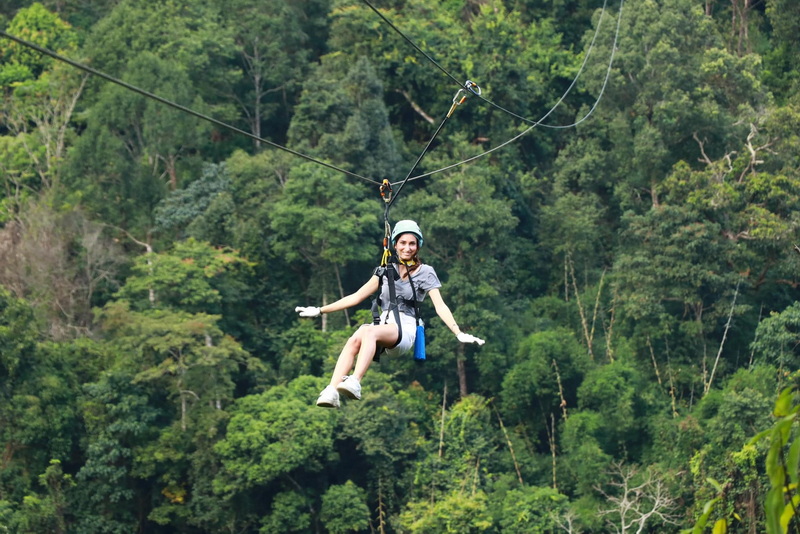 Zipline Adventure Over Forest at Kingkong Smile Zipline Woman with helmet and harness enjoying zipline over lush forest canopy at Kingkong Smile Zipline.