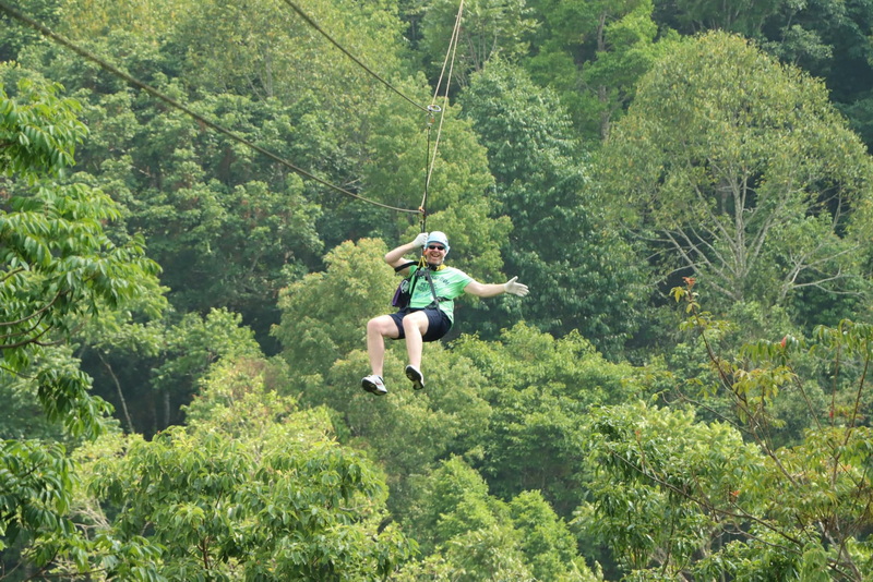Person ziplining through a lush green forest with safety gear and helmet at King Kong Smile Zipline.