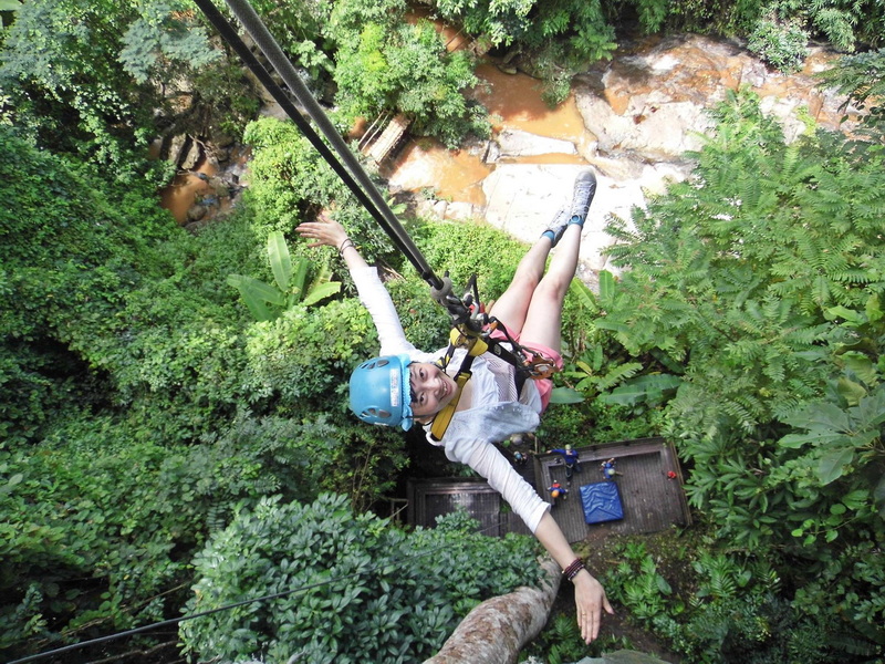 Girl with helmet ziplining over dense green forest canopy at Phoenix Zipline Chiang Mai.