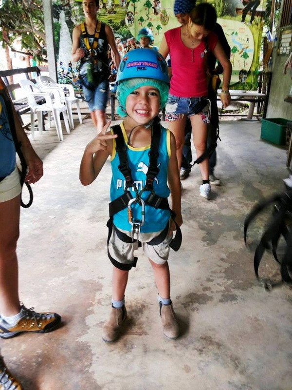 Boy with helmet and harness smiling inside an adventure park with people around at Phoenix Zipline Chiang Mai.