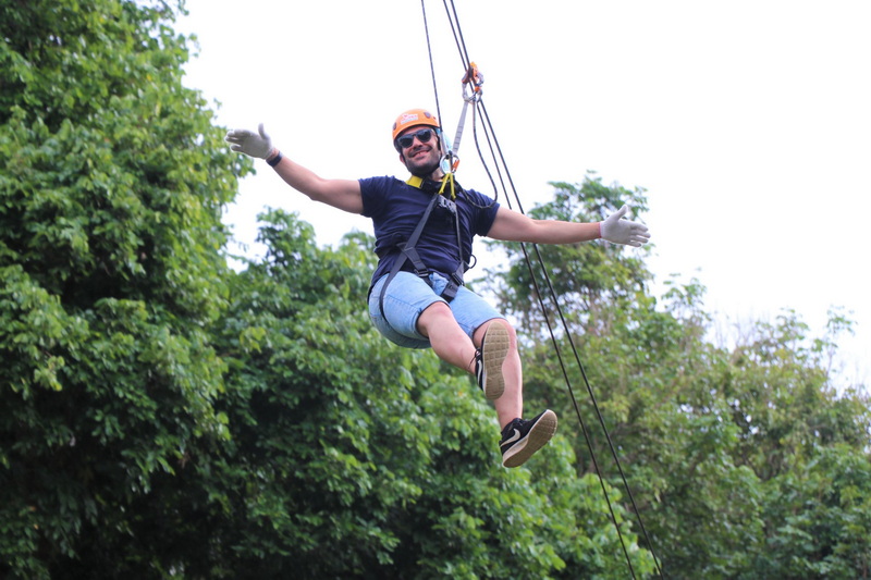 Person ziplining with helmet and harness through lush green trees outside at Phoenix Zipline Chiang Mai.