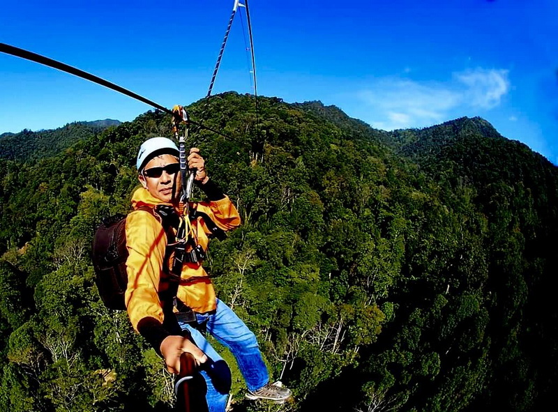 Exciting Forest Zip-lining Adventure at Phoenix Zipline Chiang Mai Person in yellow jacket and helmet zip-lining over a dense green forest under a blue sky at Phoenix Zipline Chiang Mai.