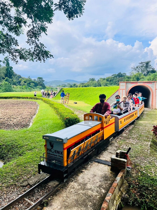 Train at Adventure Park at Phoenix Adventure Park Small train with passengers traveling through greenery near a tunnel entrance at Phoenix Adventure Park.