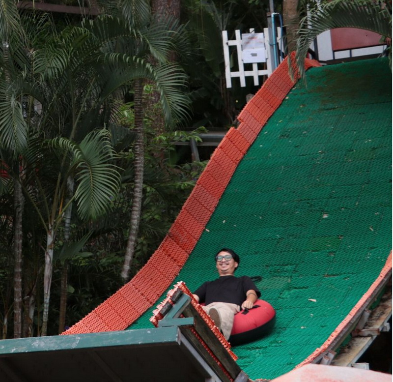 Tropical Zipline Adventure at Pong Yang Zipline Person sitting in a red inflatable tube at the start of a green and orange zipline ramp surrounded by trees at Pong Yang Zipline.