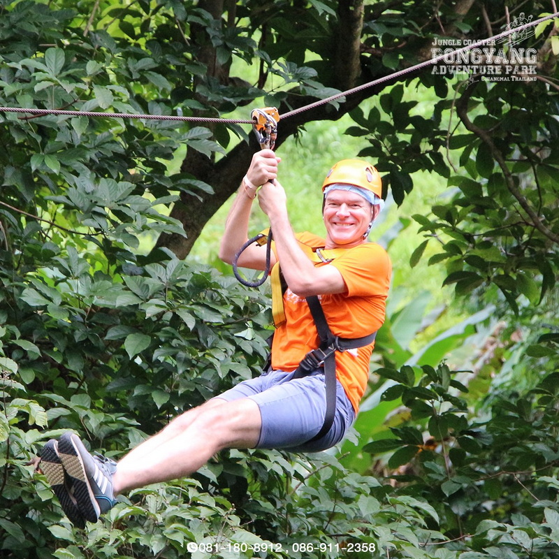 Man smiling on zipline surrounded by lush green trees during outdoor adventure at Pong Yang Zipline.