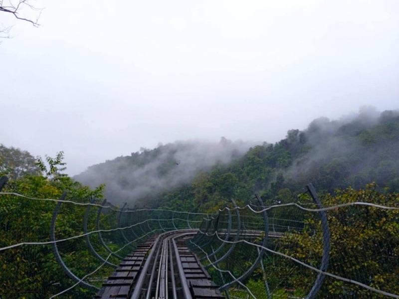 Narrow railway on a suspension bridge over a foggy, green forested valley at Pong Yang Zipline.