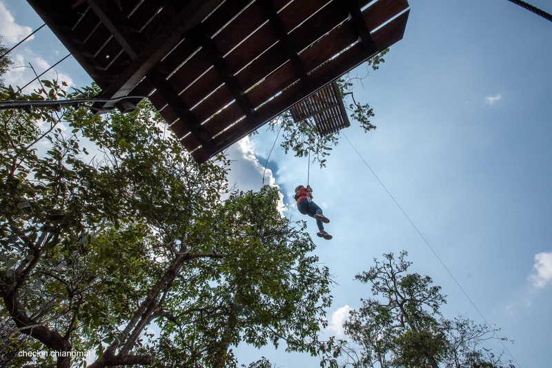 Person swinging on a zipline from a wooden platform among trees under the sky at Pong Yang Zipline.