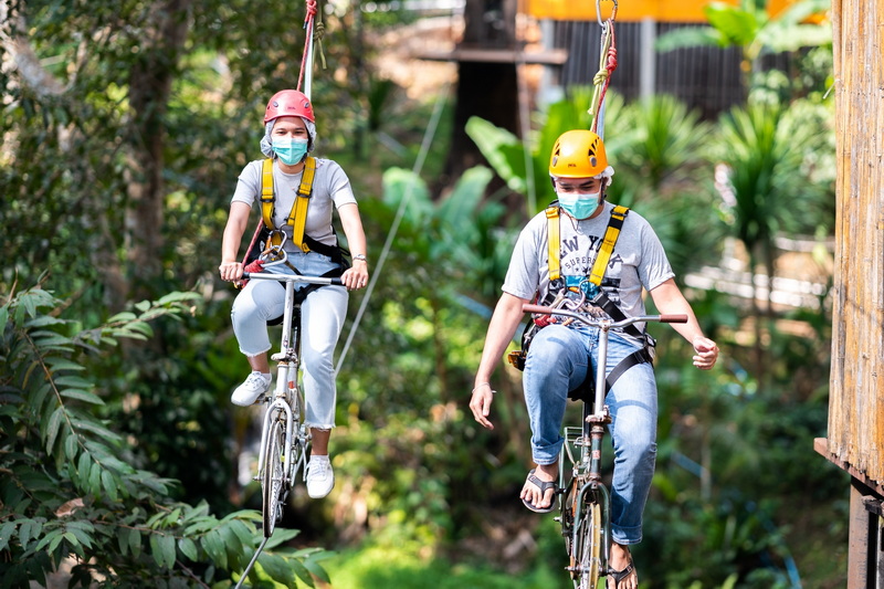 Forest Bike Ride Adventure at Pong Yang Zipline and Jungle Coaster Two individuals riding bikes on a wooden pathway surrounded by lush greenery at Pong Yang Zipline and Jungle Coaster.