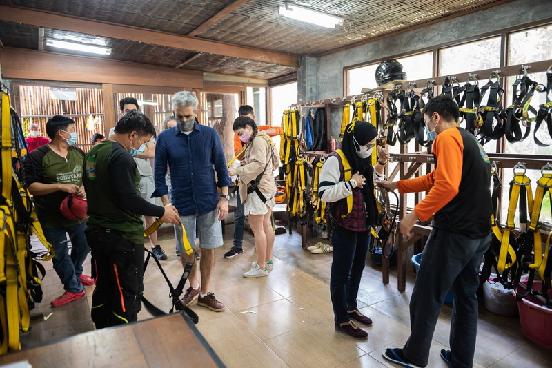 Group of people preparing ziplining harnesses indoors with safety gear on the wall at Pong Yang Zipline.