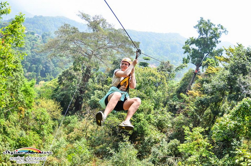 Person ziplining with a scenic green forest in the background at Skyline Jungle Luge.