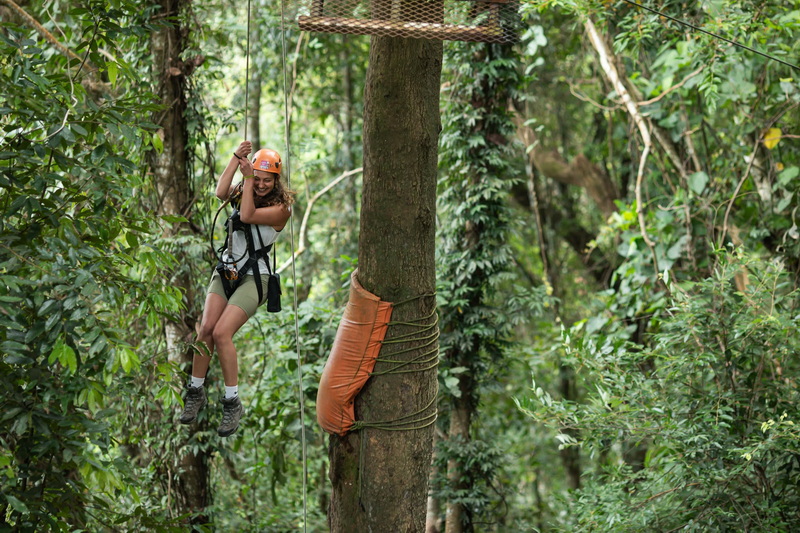 Jungle Zipline Adventure at Chiang Mai Skyline Adventure Woman in safety gear swinging on zipline amid lush trees at Chiang Mai Skyline Adventure.