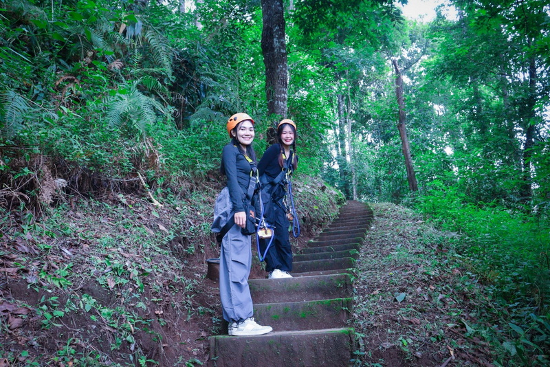 Two women in helmets and harnesses on a forest staircase smiling at the camera at Chiang Mai Skyline Adventure.