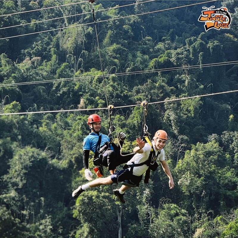 Two individuals enjoy zip lining over a lush forest canopy with safety gear at Skyline Jungle Luge.