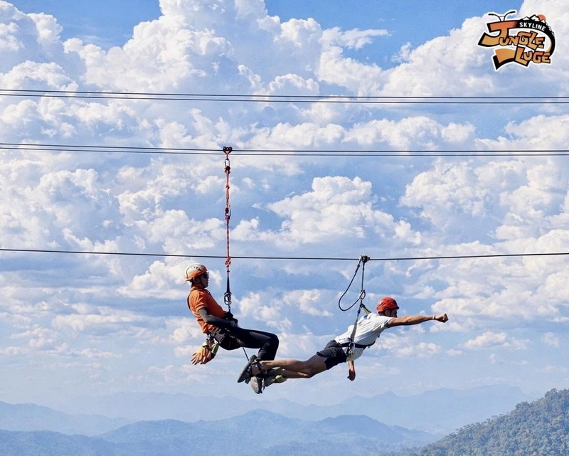Two individuals ziplining through the sky with mountain views and a scenic sky behind them at Chiang Mai Skyline Adventure.