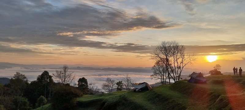 Sunrise illuminating the mountainous landscape, with tents set up among the trees at Doi Luang Chiang Dao.