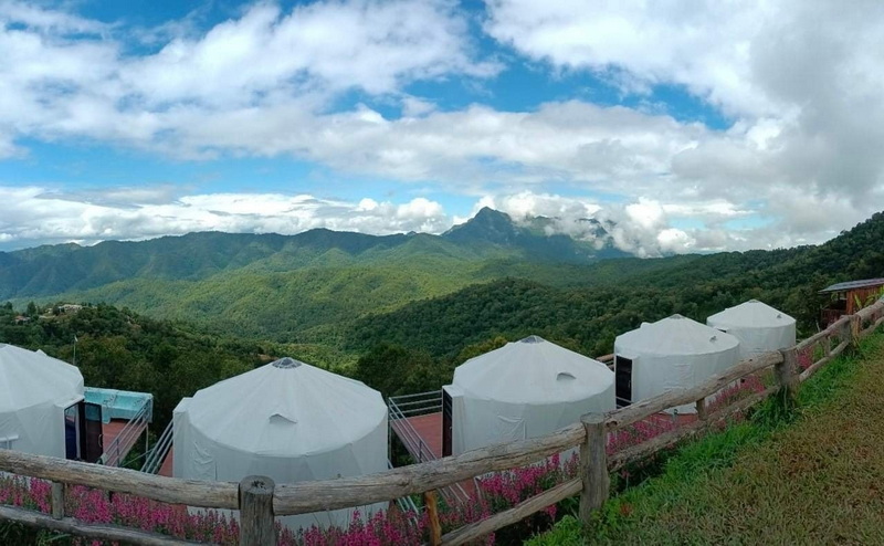 Mountain View with Tents at Doi Luang Chiang Dao White tents on a grassy slope with mountains and a cloudy sky behind at Doi Luang Chiang Dao.