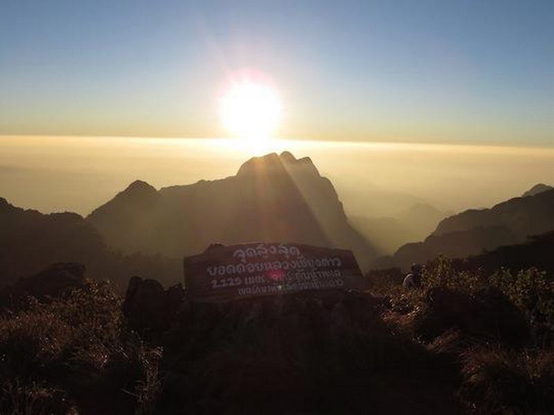Sunset Over Mountain Peaks at Doi Luang Chiang Dao Sunset over mountain peaks with clouds and a sign in foreground at Doi Luang Chiang Dao.