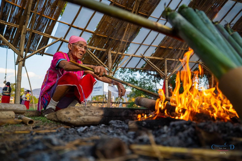 Traditional Bamboo Fire Tending at New Year Countdown Chiang Mai by CAD Elderly person tending bamboo over a fire under a bamboo shelter at New Year Countdown Chiang Mai by CAD.