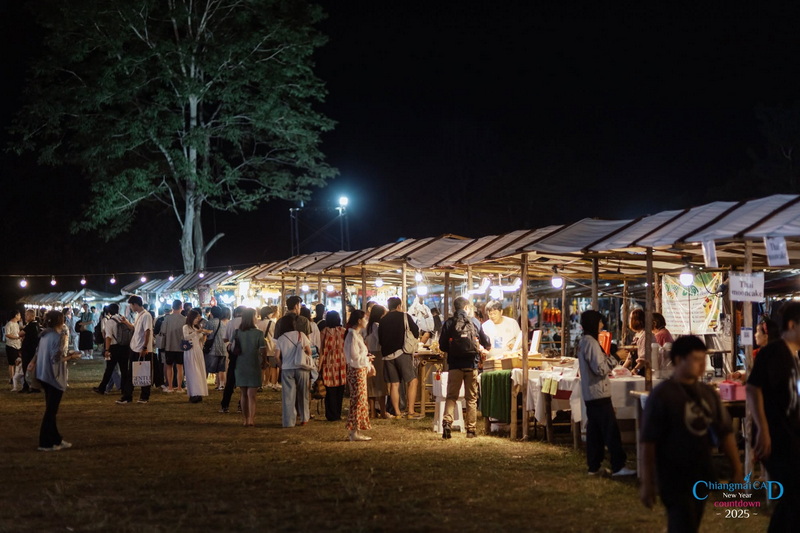 Night market with people browsing stalls under a large tree and string lights at New Year Countdown Chiang Mai by CAD.