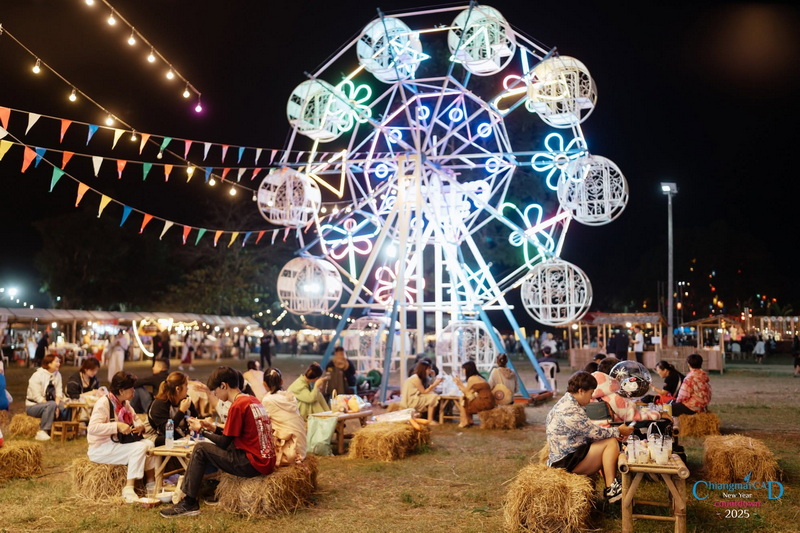 Night Festival with Ferris Wheel at New Year Countdown Chiang Mai by CAD People enjoying night festival with a lit Ferris wheel and string lights at an outdoor event at New Year Countdown Chiang Mai by CAD.