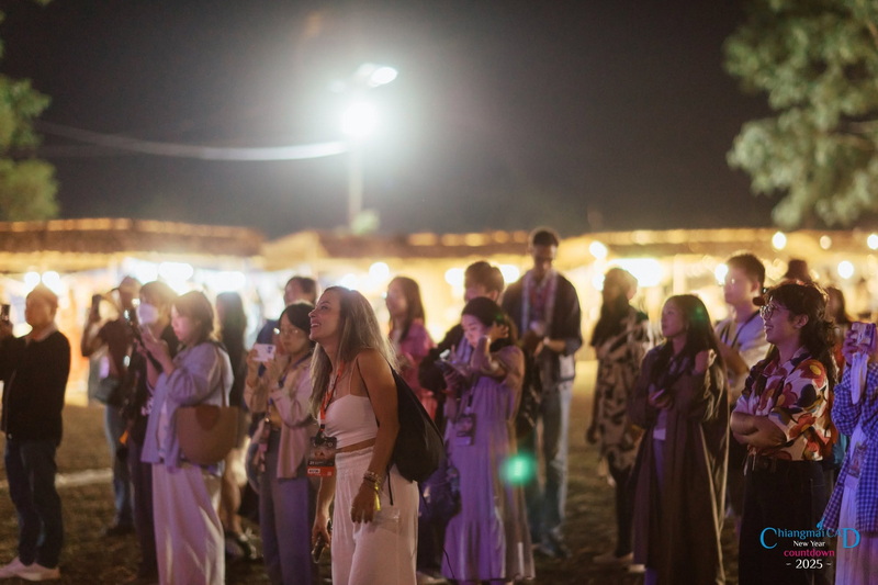 People gathered at night with food stalls and bright lights behind them at New Year Countdown Chiang Mai by CAD.
