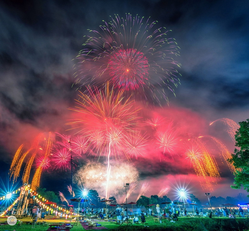 Fireworks exploding in the night sky over a festive outdoor gathering at New Year Countdown Chiang Mai by CAD.