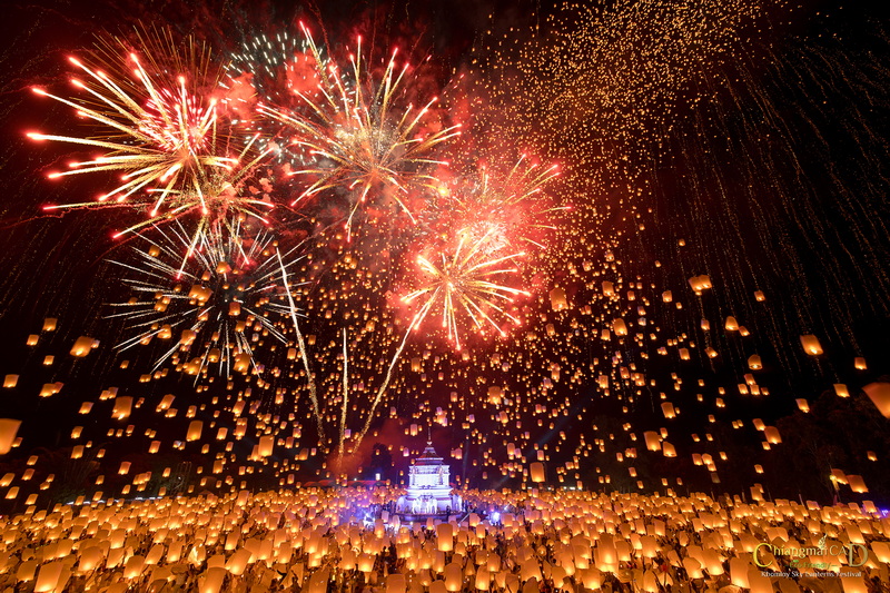 Colorful fireworks explode above a temple with floating lanterns at night at Yi Peng Chiang Mai.