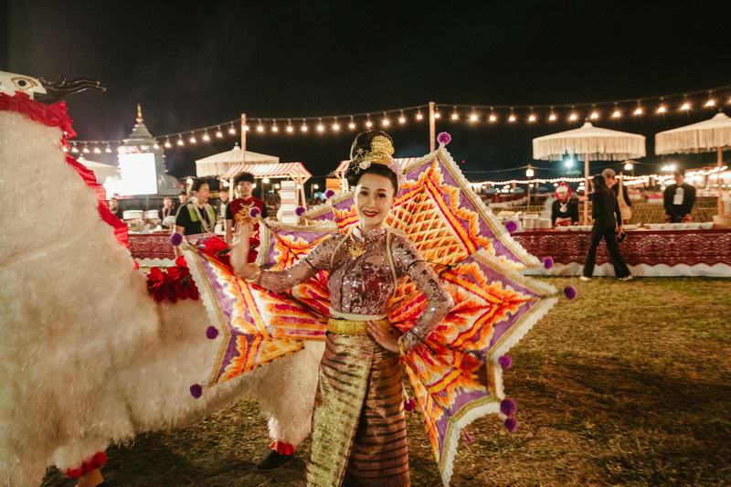 Woman in traditional Thai dress standing next to a decorative llama at night festival at Festivals.