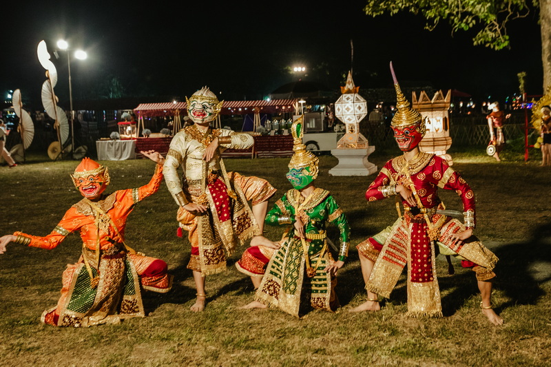 Five performers in colorful costumes and masks pose outdoors at night at Yi Peng Chiang Mai.