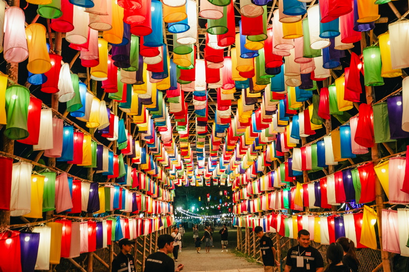 Colorful Lantern Festival Scene at Yi Peng Chiang Mai Colorful lanterns hanging in a festival setting with people walking underneath at night at Yi Peng Chiang Mai.