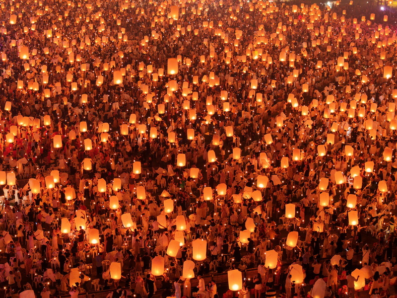 Crowd holding glowing lanterns illuminated at night during a festival at Yi Peng Chiang Mai.