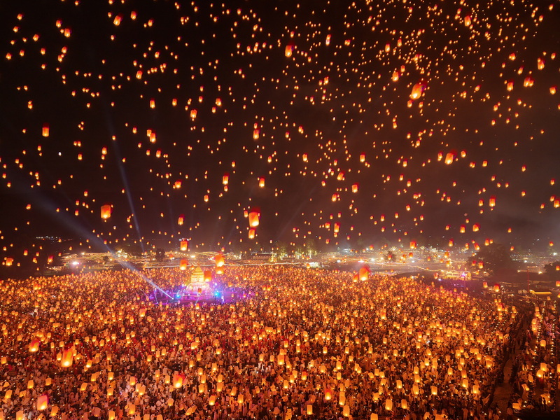 Hundreds of floating lanterns glowing in the night sky over a large crowd during a festival at Yi Peng Chiang Mai.