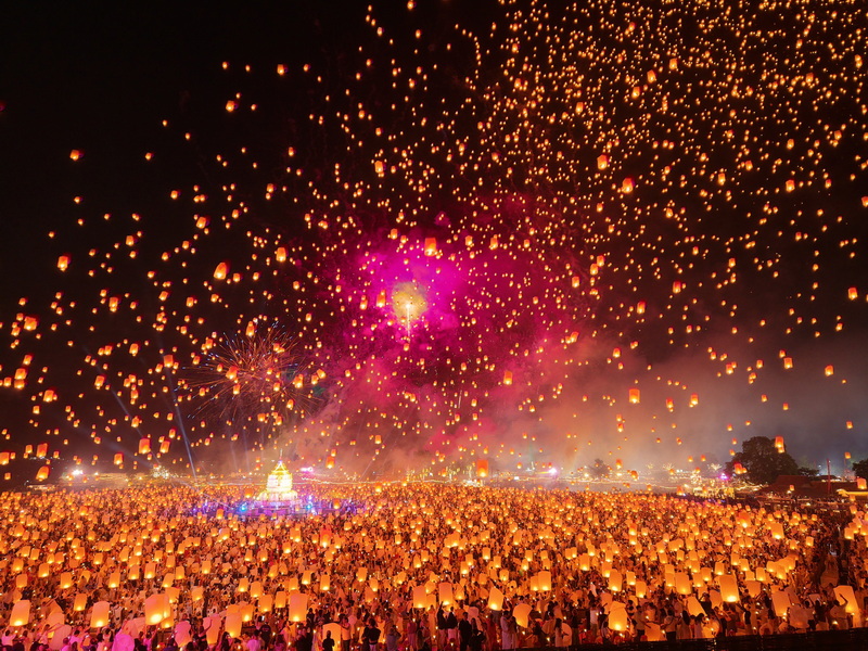 Night sky filled with floating lanterns and fireworks above a large crowd at Yi Peng Chiang Mai.