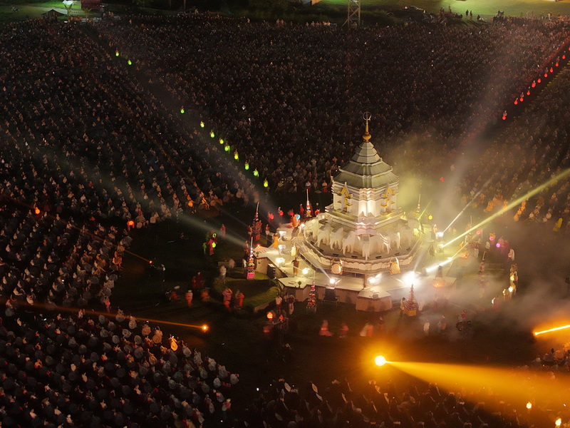 Night scene with a large crowd and illuminated monument with fog effects at Yi Peng Chiang Mai.