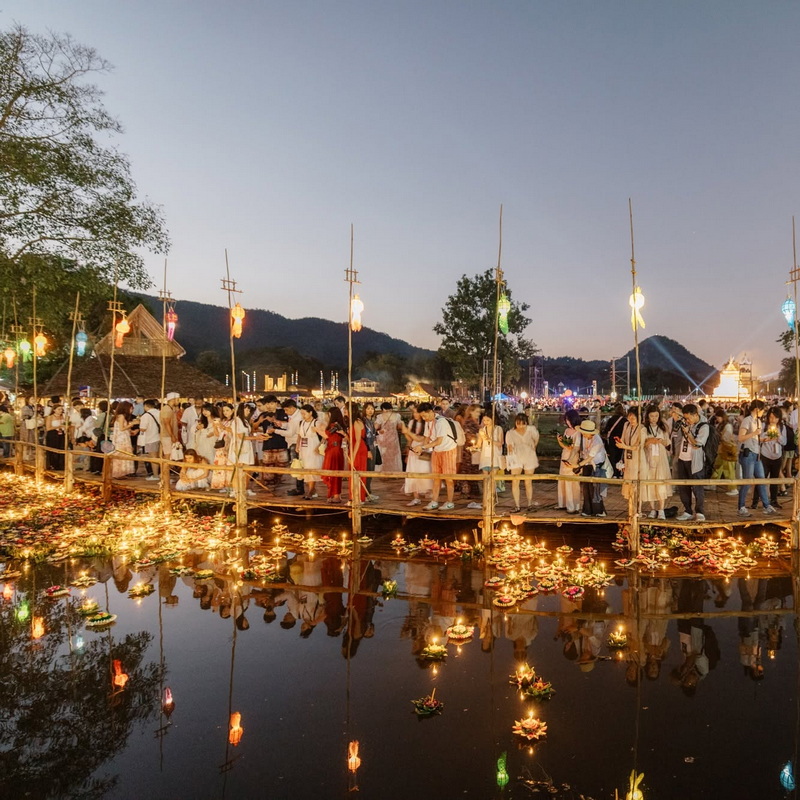 Crowd of people and floating lanterns over a pond during festival at dusk at Yi Peng Chiang Mai.