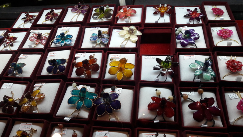 Display of vibrant flower-shaped jewelry pieces in red boxes, showcasing colorful gemstones at Chiang Mai Orchid.