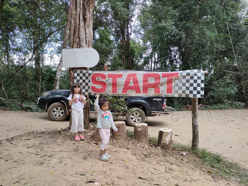 Children at Trail Start at Mon Jam Two girls standing near a start banner with cars and trees in the background at Mon Jam.