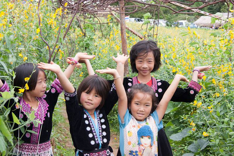 Four children happily posing among yellow flowers in a garden or field at Mon Jam.