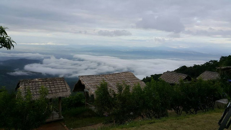 Huts on a hillside with a cloudy sky and distant mountains in the background at Mon Jam.