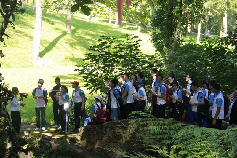 Students in uniform standing in a lush green park with tall trees and grass at Queen Sirikit Botanic Garden.