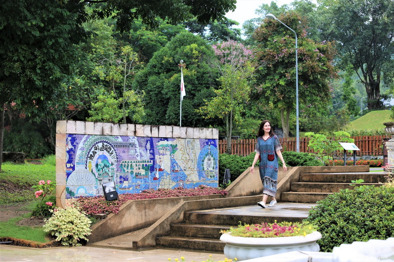 Garden Mosaic Wall Scene at Chiang Mai Gardens Woman walking down steps in a garden with a colorful mosaic wall and trees in the background at Chiang Mai Gardens.