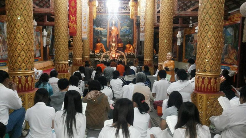 Inside a Buddhist Temple Hall at Kruba Sri Wichai Monument People seated inside a richly decorated temple with a golden altar and paintings at Kruba Sri Wichai Monument.