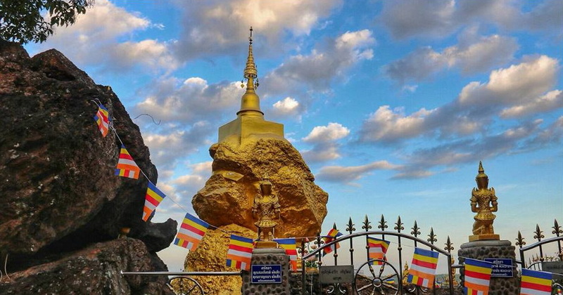 Golden Stupa with Prayer Flags at Phra That in Kwaen Golden stupa with prayer flags and rocks under a blue sky with clouds at Phra That in Kwaen.