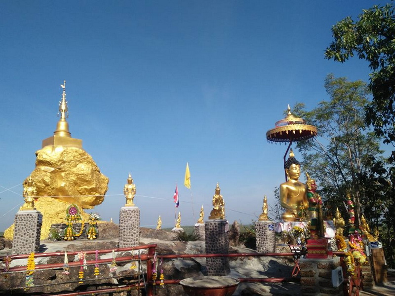 Golden Buddha Statues at Sacred Site at Wat Phra That in Kwaen Golden Buddha statues and offerings on a rocky platform with flags and floral decorations at Wat Phra That in Kwaen.