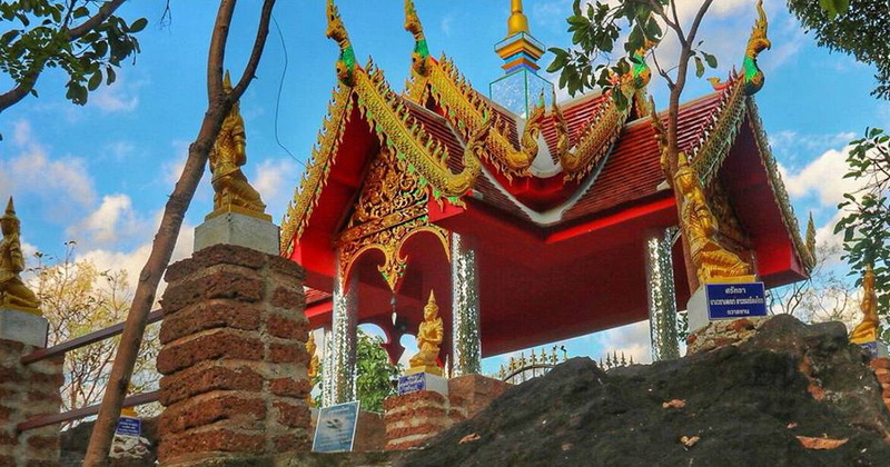 Traditional Thai pavilion with intricate gold and red decorations under a blue sky at Wat Phra That in Kwaen.